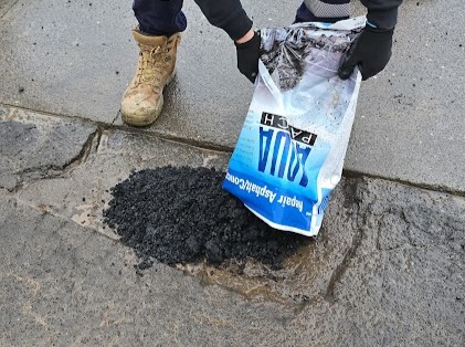 Aqua Patch bag beside a pile of the aggregate product at the edge of a pothole